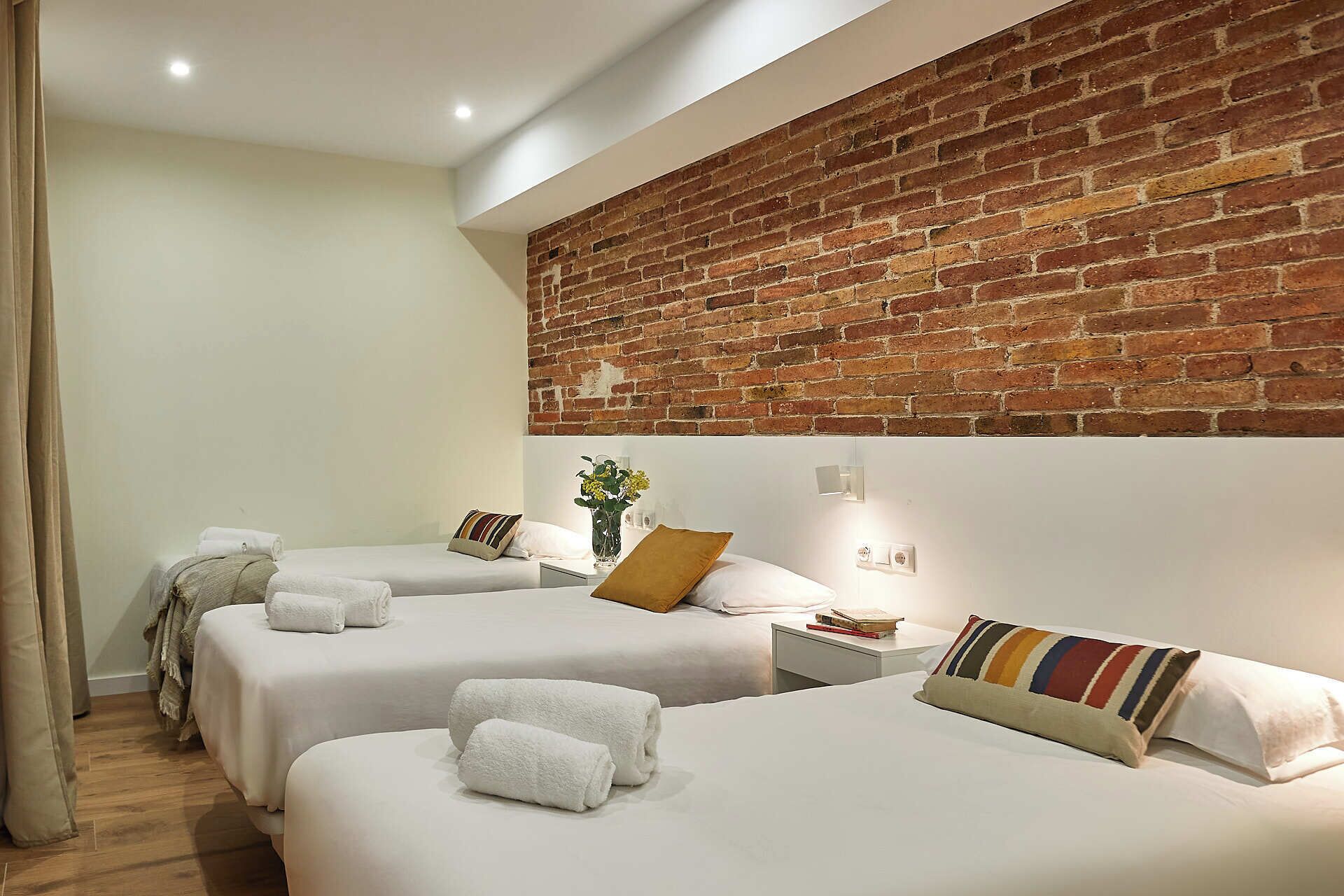 Habitación de hotel con dos camas, una pared decorativa de ladrillo y una mesita de noche con un jarrón de flores.