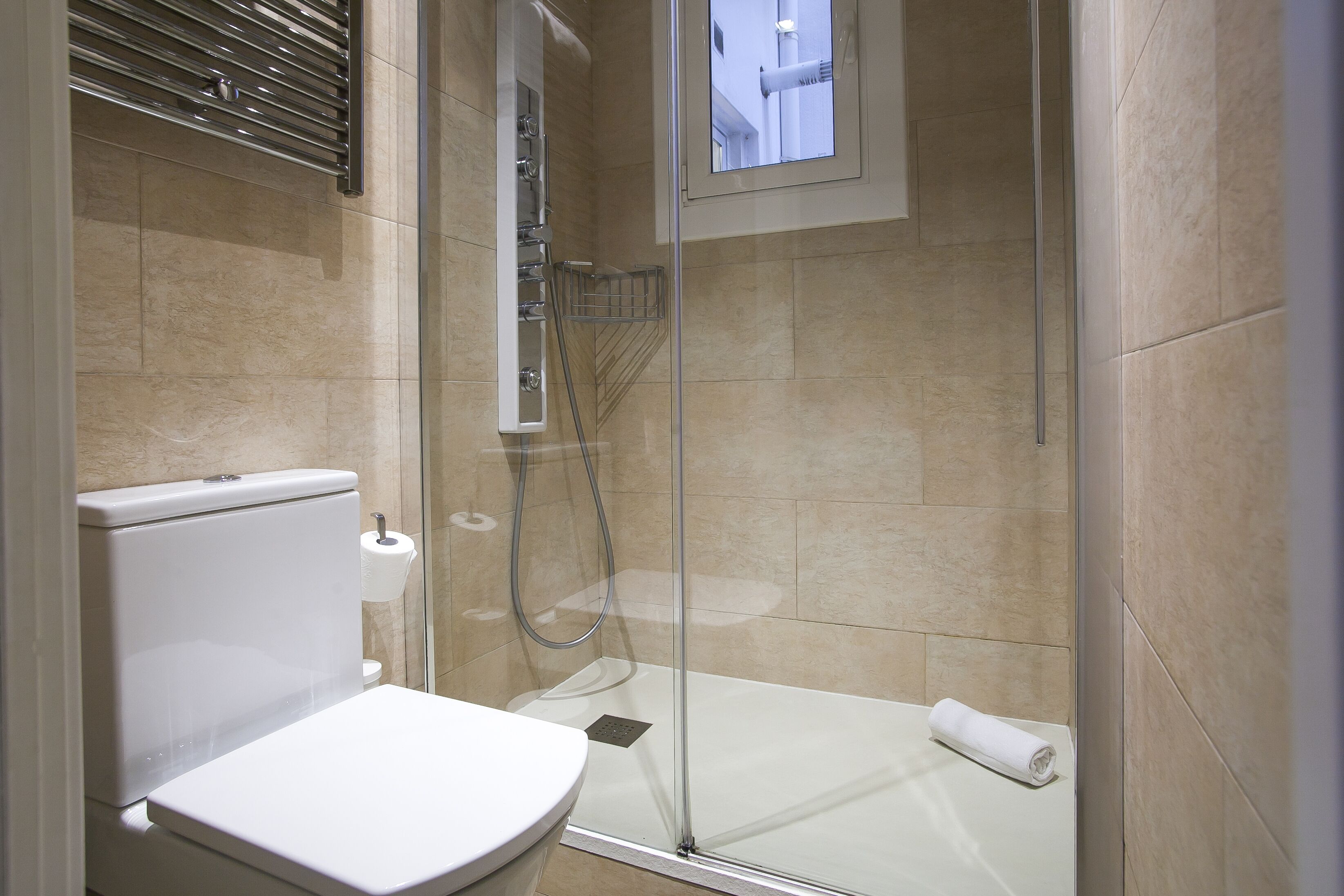 A modern bathroom with a glass-enclosed shower, a toilet, and a towel on the floor.