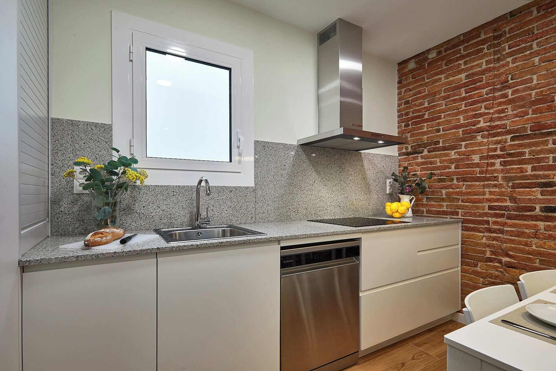 A modern kitchen with granite countertops, a stainless steel dishwasher, and a brick accent wall.
