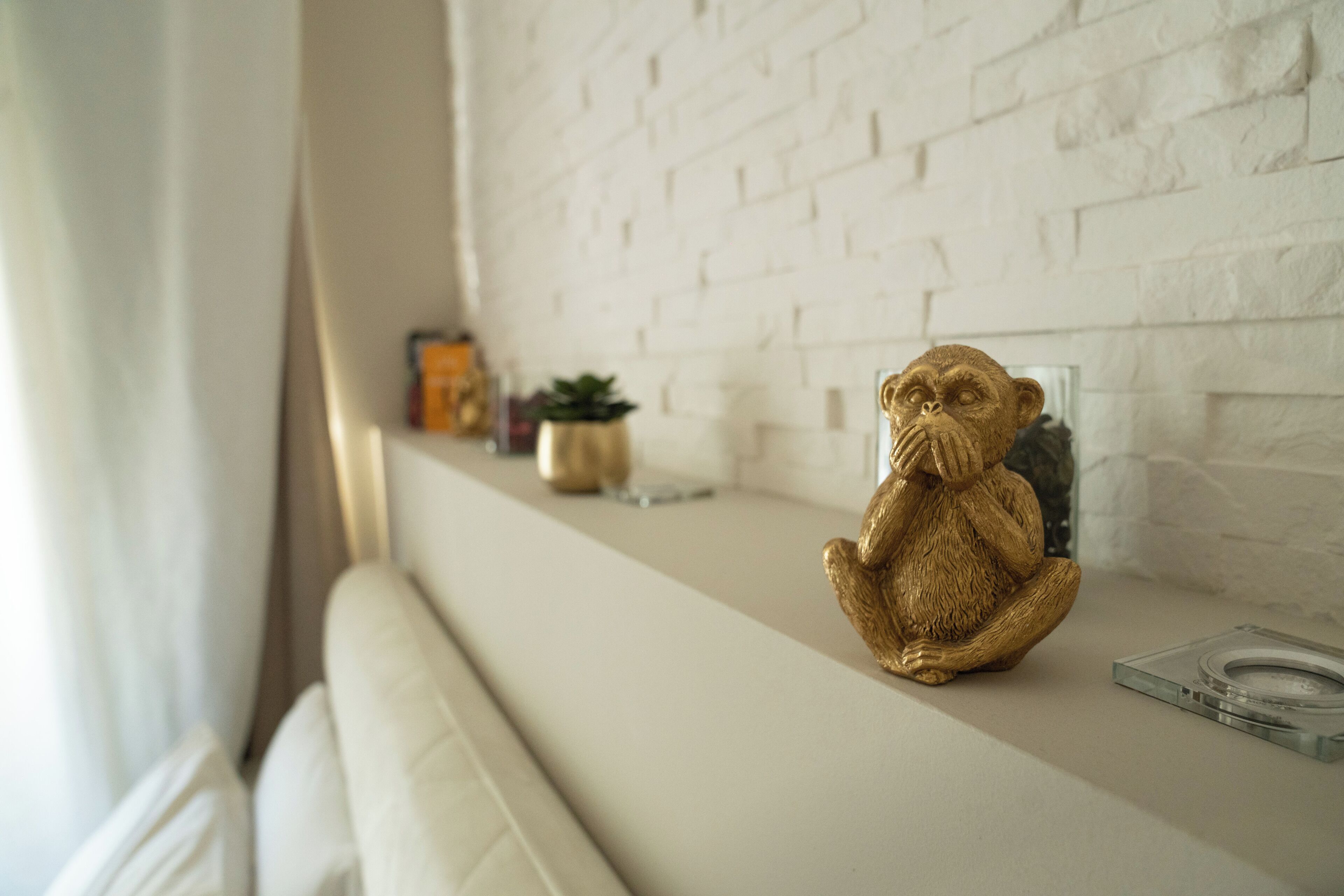 Una habitación con pared de ladrillo blanco, un sofá blanco y una pequeña figurina de un mono en un estante.