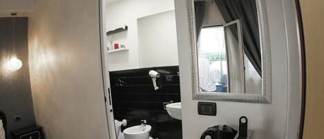 A hotel room with a bed, a desk with a coffee maker, a mirror, and an air conditioning unit.