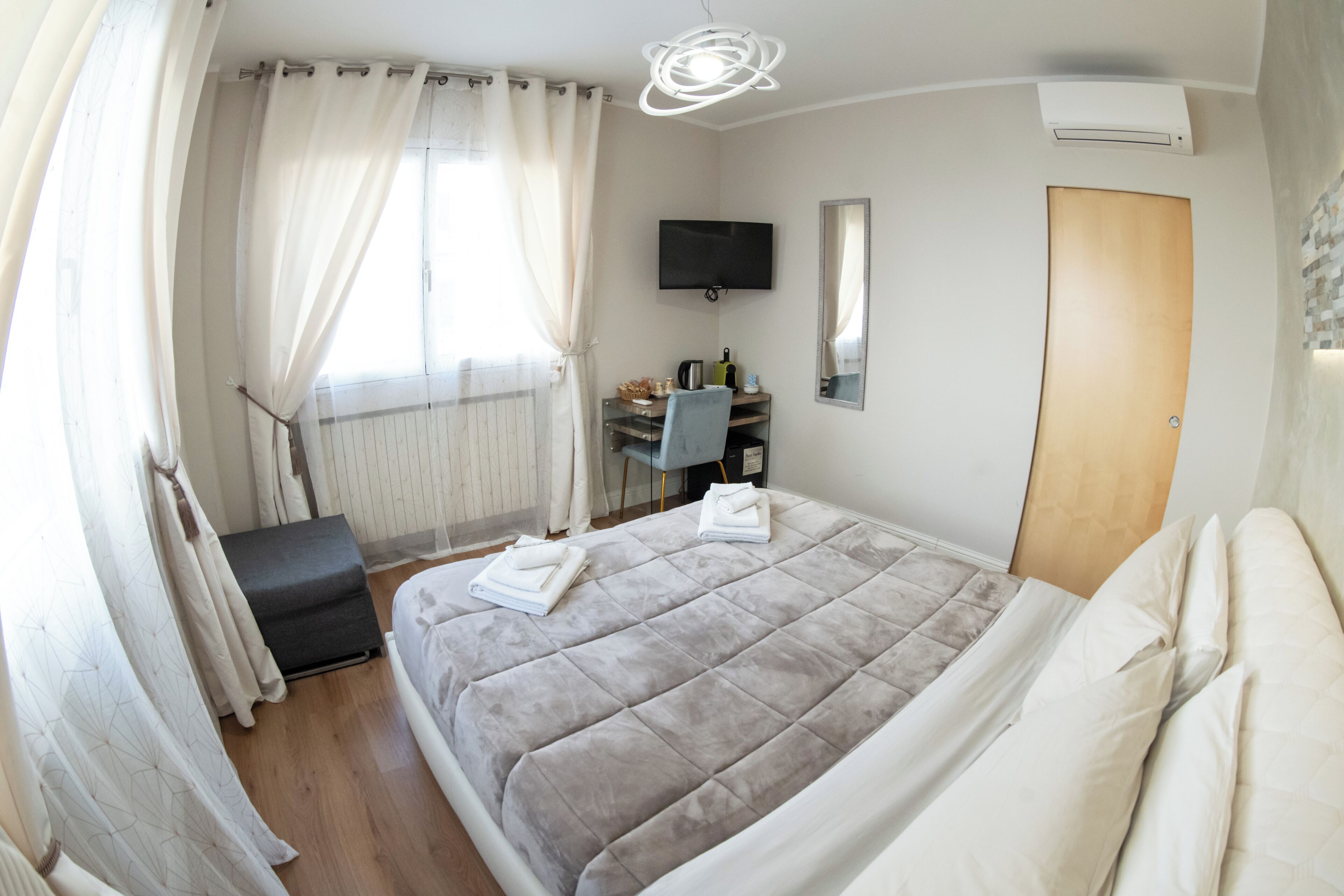 Una habitación de hotel moderna con una cama grande, un escritorio, una silla, un televisor y un armario.