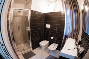 Moderni kylpyhuone, jossa on lasiseinäinen suihkukaappi, wc, bidee ja pesuallas.