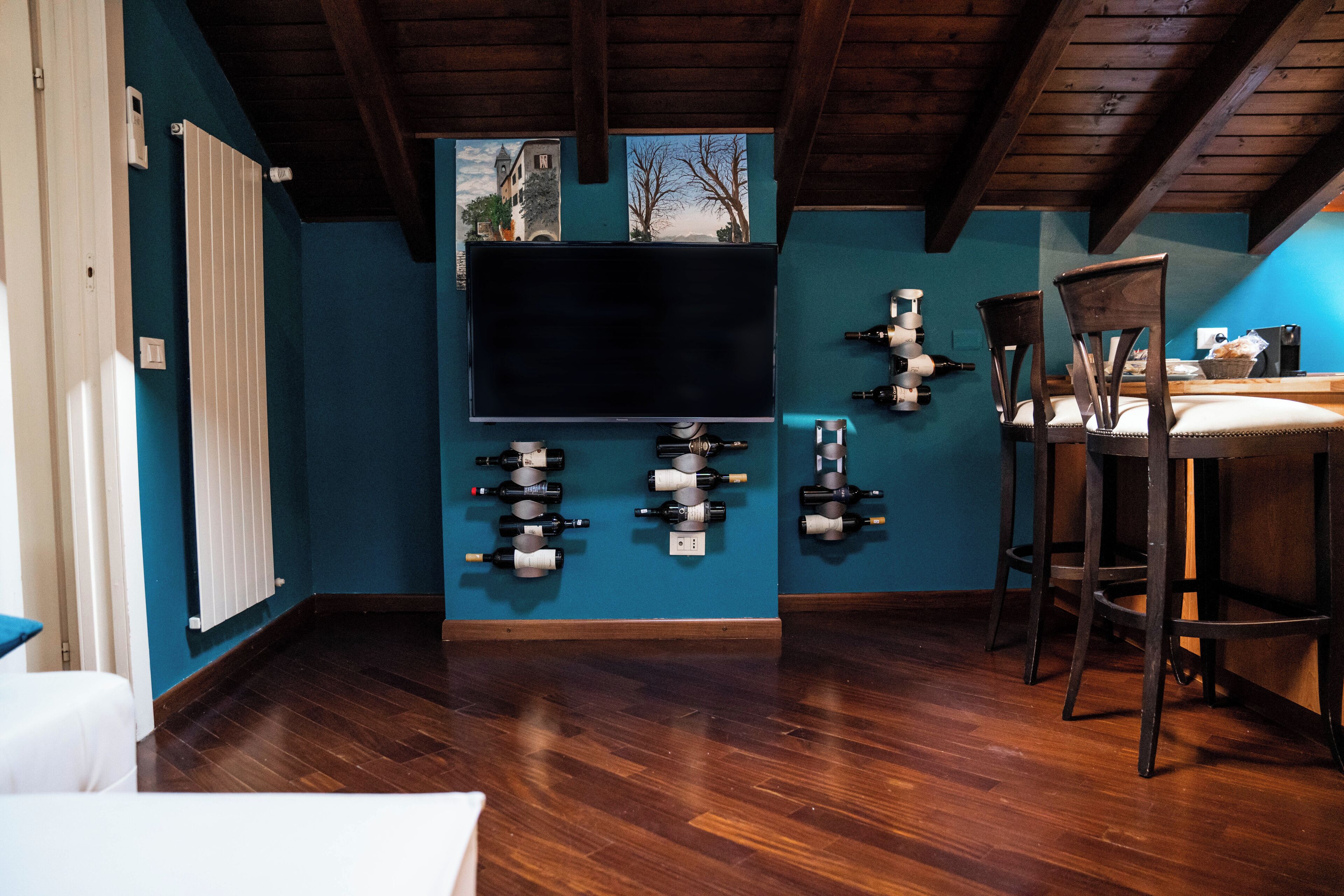 Ein Zimmer mit Holzbalkendecke, einem an der Wand befestigten Fernseher und einer Weinregalanlage.