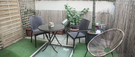 Un patio con una mesa redonda, dos sillas, una mesita y una planta en maceta.