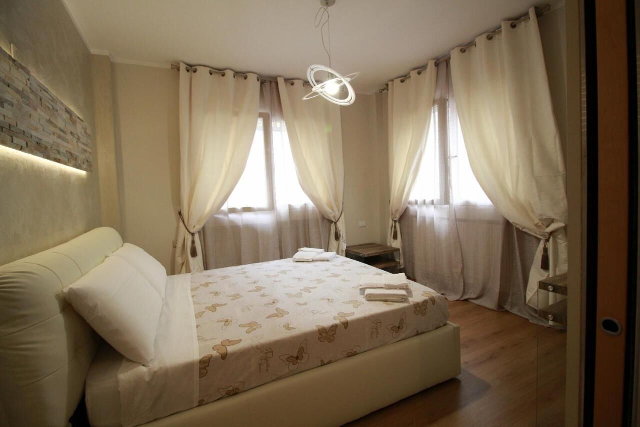 A bedroom with a bed, curtains, a nightstand, and a wall-mounted light fixture.