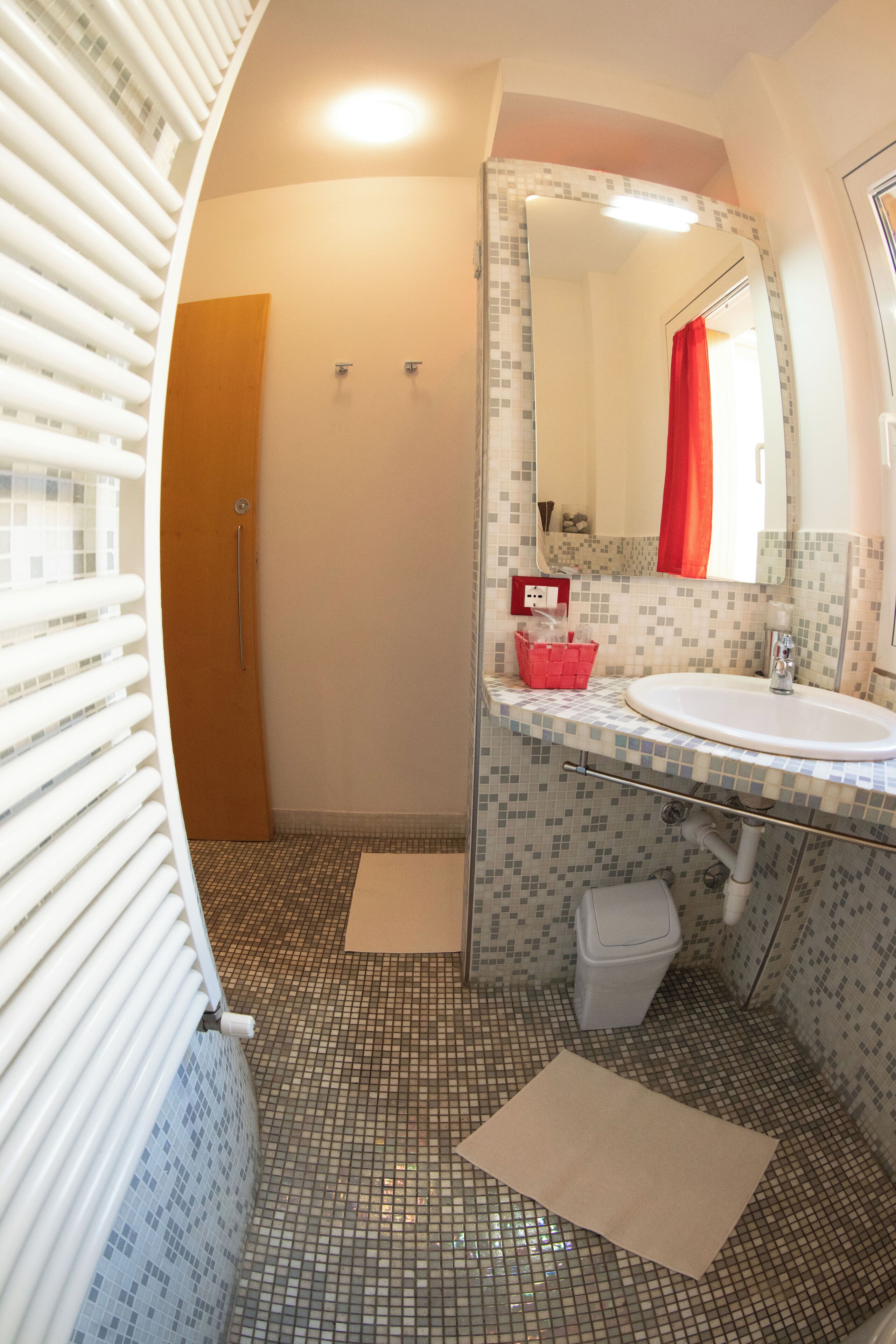 A bathroom with a tiled floor, a sink, a mirror, and a shower area.