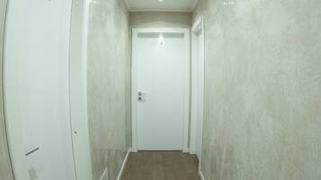 Un pasillo con pared de mármol, suelo de madera y una puerta blanca al final.