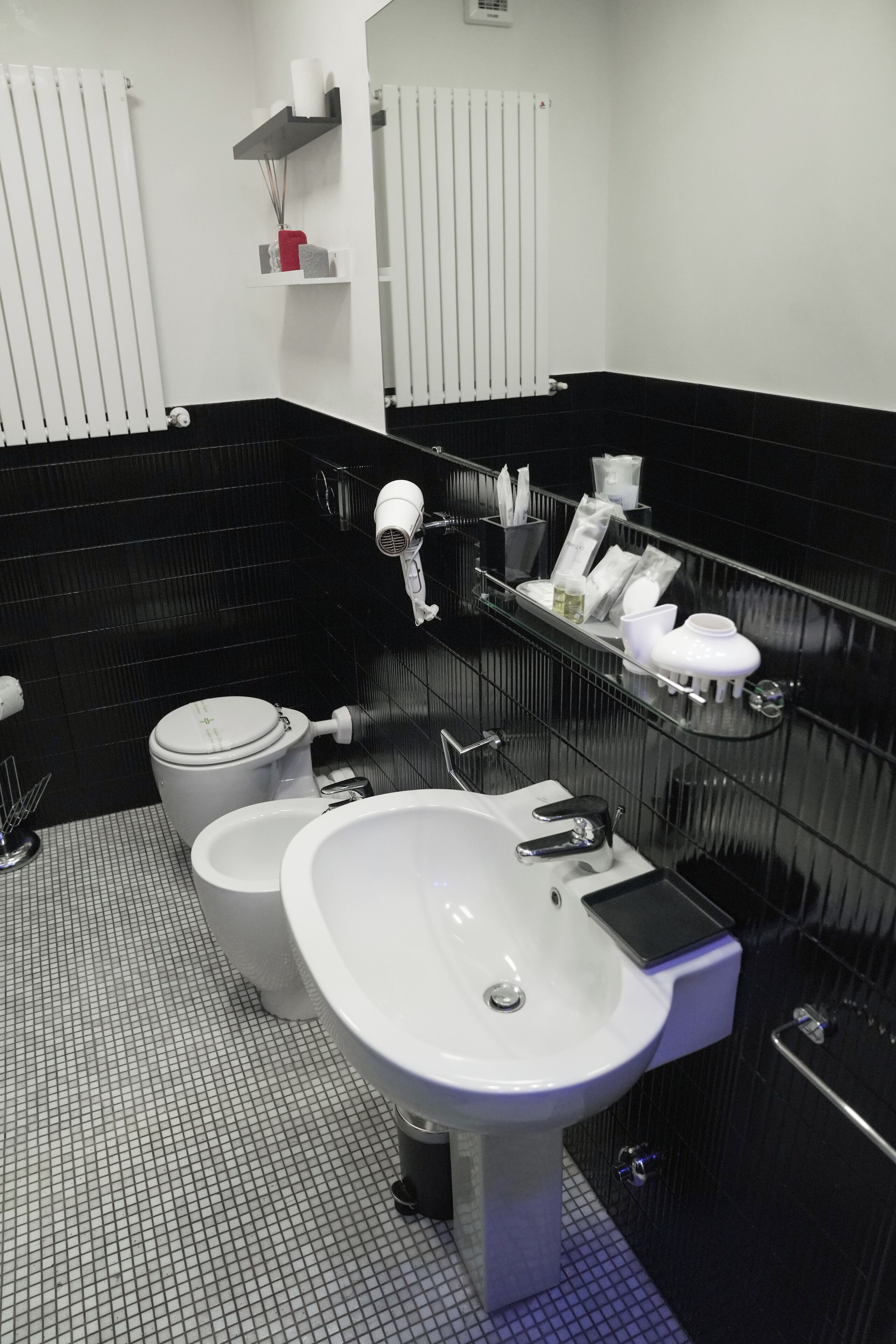 Ein modernes Badezimmer mit Toilette, Bidet und Waschbecken. Über dem Waschbecken befinden sich Ablageflächen und an der Wand ein Spiegel.