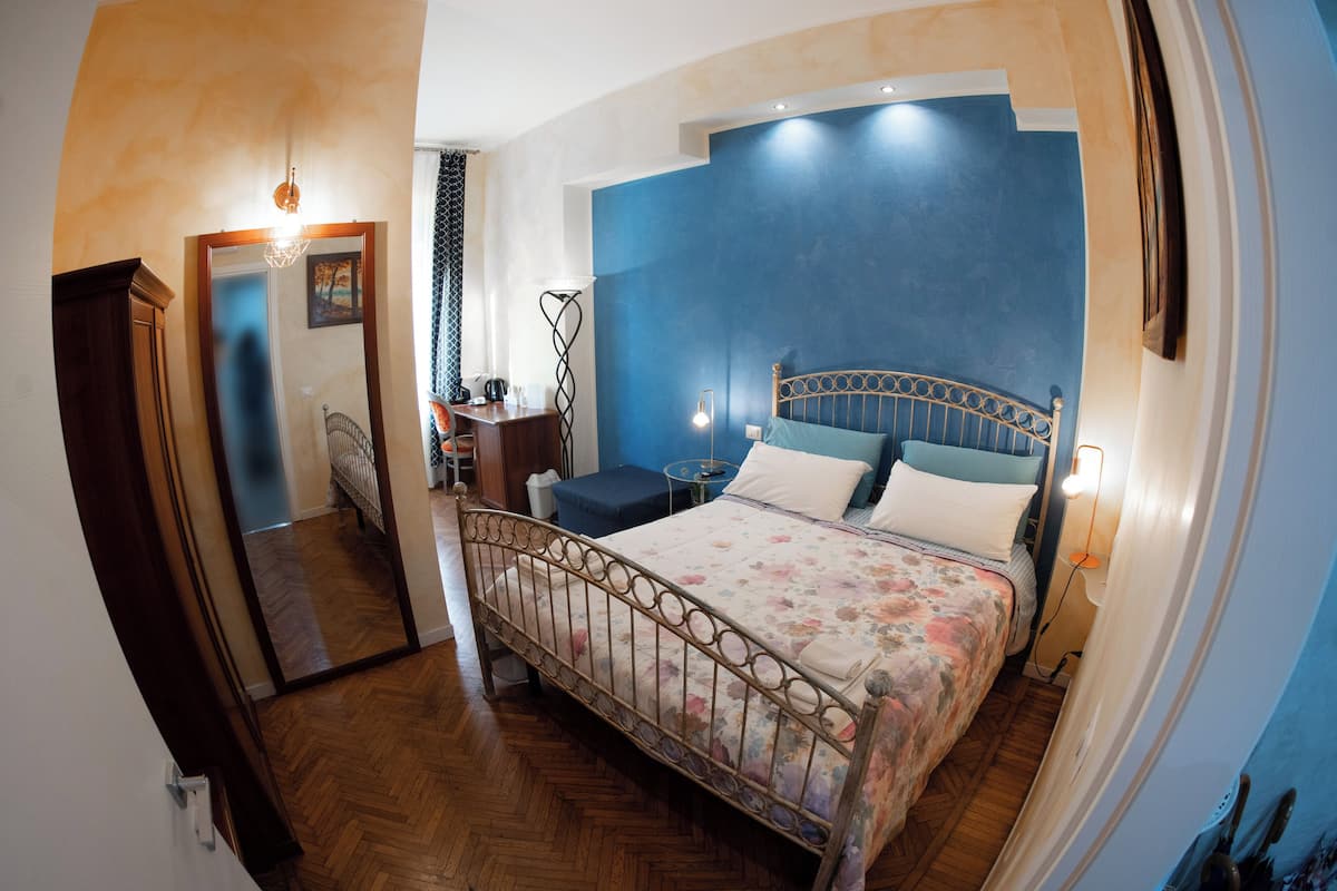 A bedroom with a bed, bedside table, lamp, and a mirror.