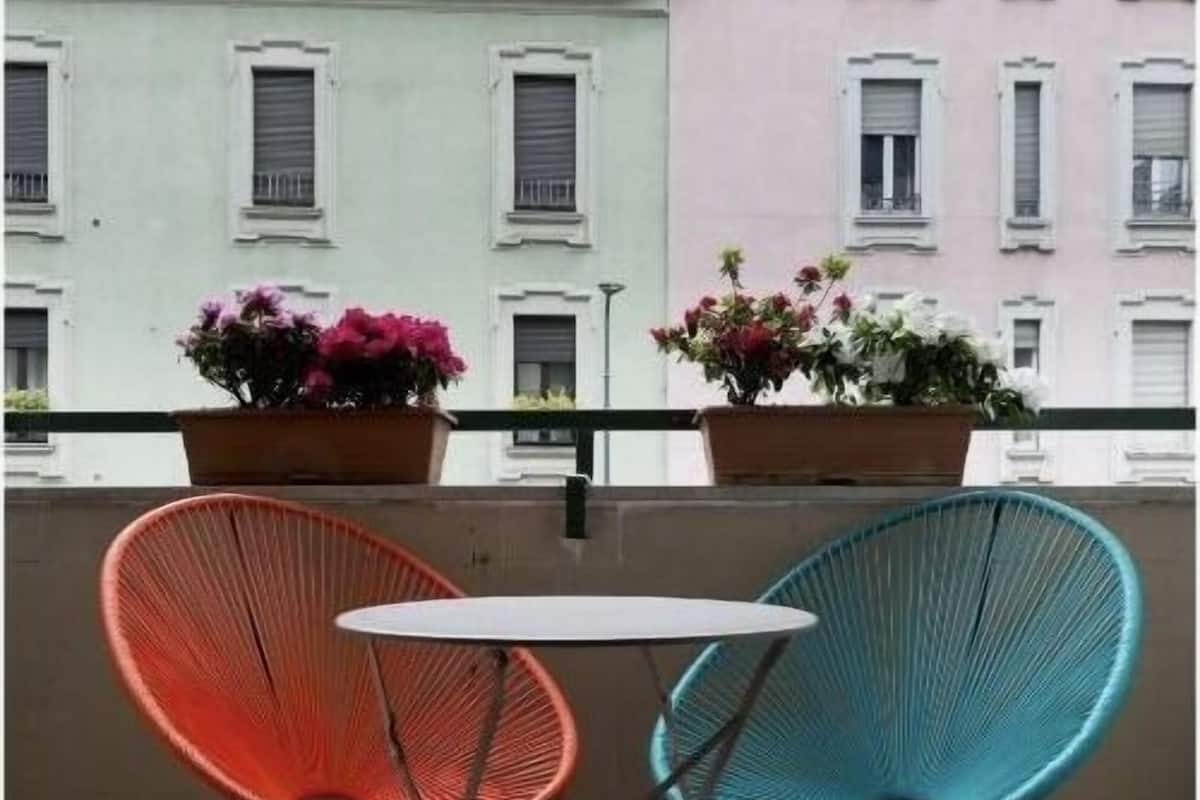 A balcony with two chairs and a table, overlooking a row of pastel-colored buildings.