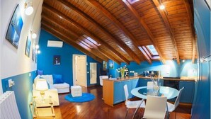 A spacious room with a wooden ceiling, a dining area with a round table and chairs, a kitchen with blue cabinets, and a blue accent wall. - La Residenza Isabella (Milan)