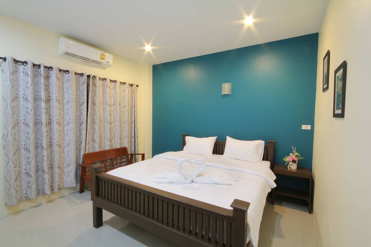 A neatly made bed with white linens and a heart-shaped towel arrangement, a wooden headboard, a nightstand with a vase, and a blue accent wall.