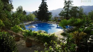 A pool area with lounge chairs and umbrellas, surrounded by lush greenery and trees. - Termas Jahuel Hotel & Spa (Santa Maria)