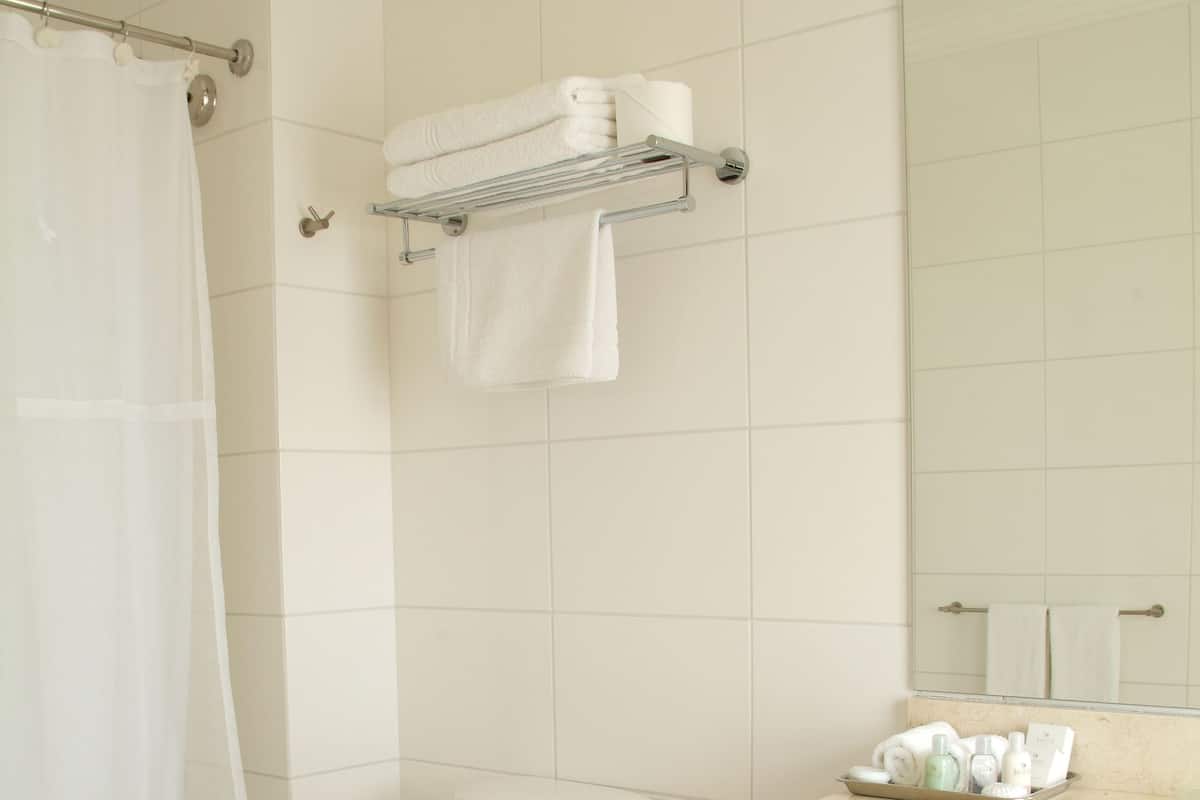 A bathroom with a toilet, a shower curtain, a towel rack with towels, a sink with toiletries, and a mirror.
