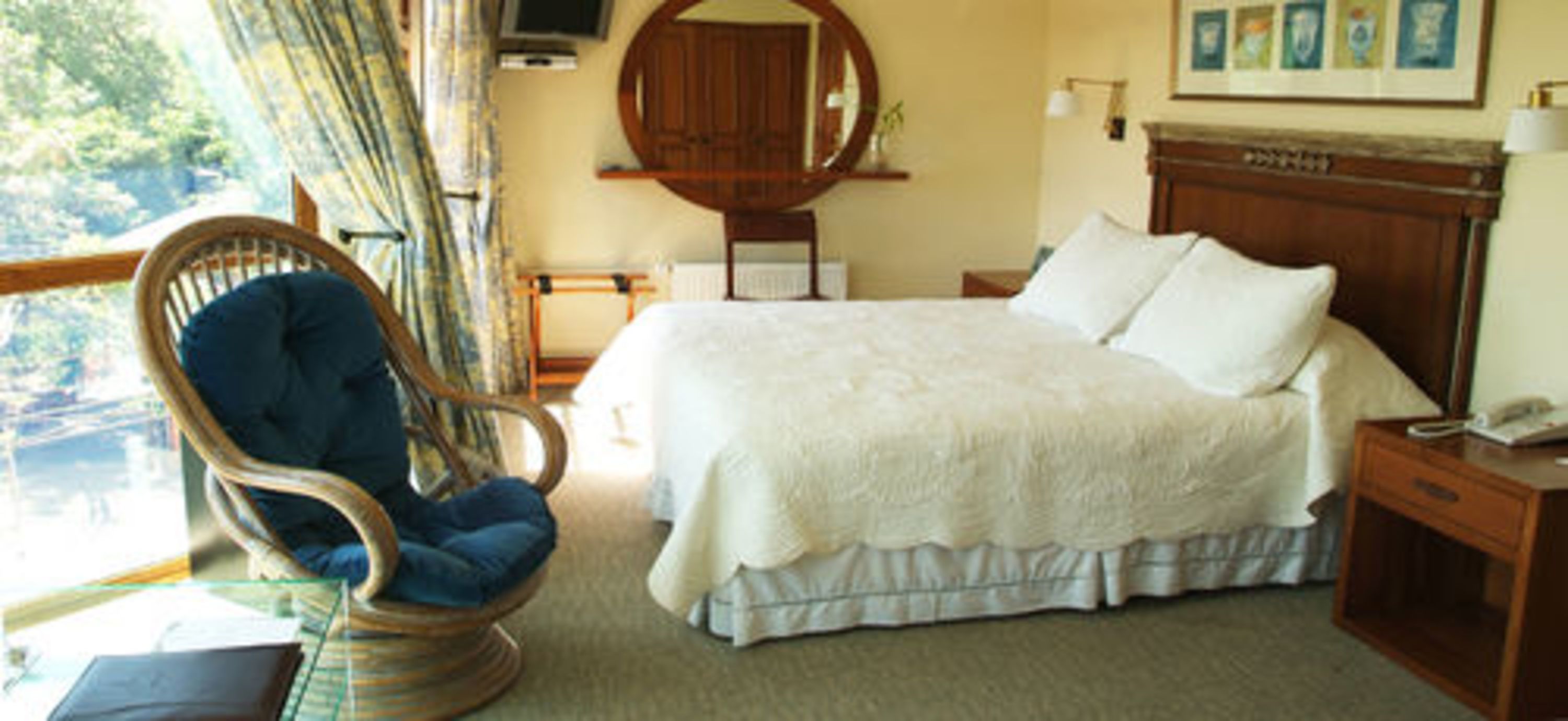 A bedroom with a large bed, a wooden headboard, a wooden nightstand, a chair, and a window with curtains.