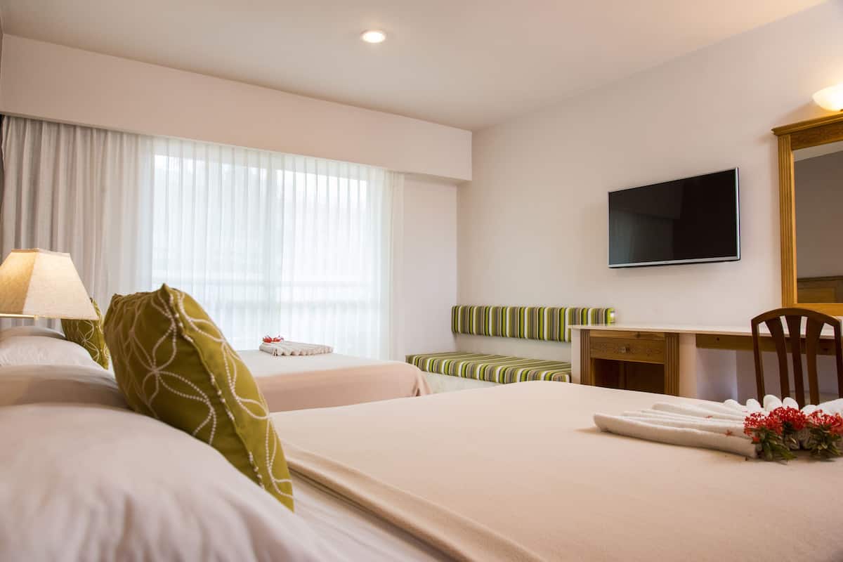 A hotel room with two beds, a desk, a chair, a TV, and a window with curtains.