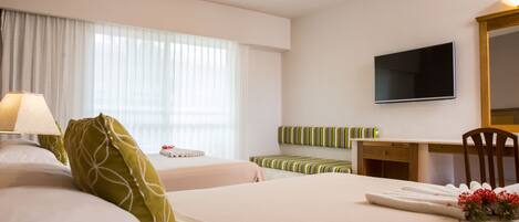 Una habitación de hotel con dos camas, un escritorio, una silla, un televisor y una ventana con cortinas.