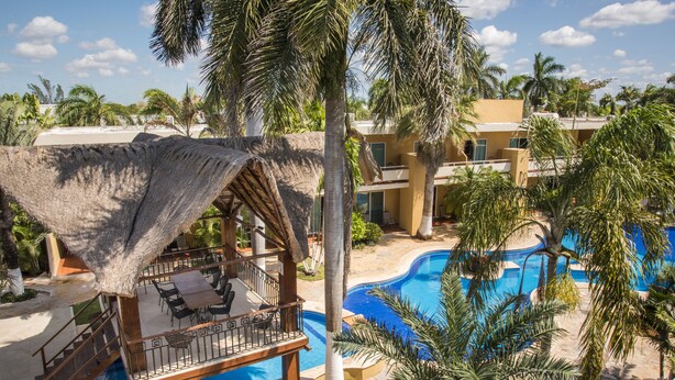 A resort with a pool, palm trees, and a thatched-roof lounge area. - TecnoHotel Mérida Norte (Mérida)