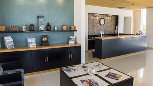 A reception area with a counter, magazines on a coffee table, and a wall-mounted clock. - TecnoHotel Mérida Norte (Mérida)