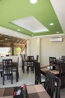 Un restaurante con techo verde, mesas y sillas de madera y plantas en macetas.