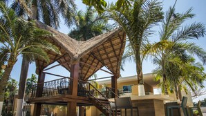 A thatched-roof outdoor area with a pool, palm trees, and a bar area with chairs. - TecnoHotel Mérida Norte (Mérida)