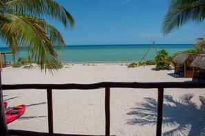 A beach with a wooden railing, a red kayak, and thatched-roof huts. - Tecnohotel Beach (Dzemul)