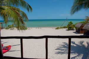 A beach with a wooden railing, a red kayak, and thatched-roof huts.
