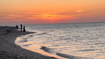 Una playa con una costa curva y un atardecer al fondo.