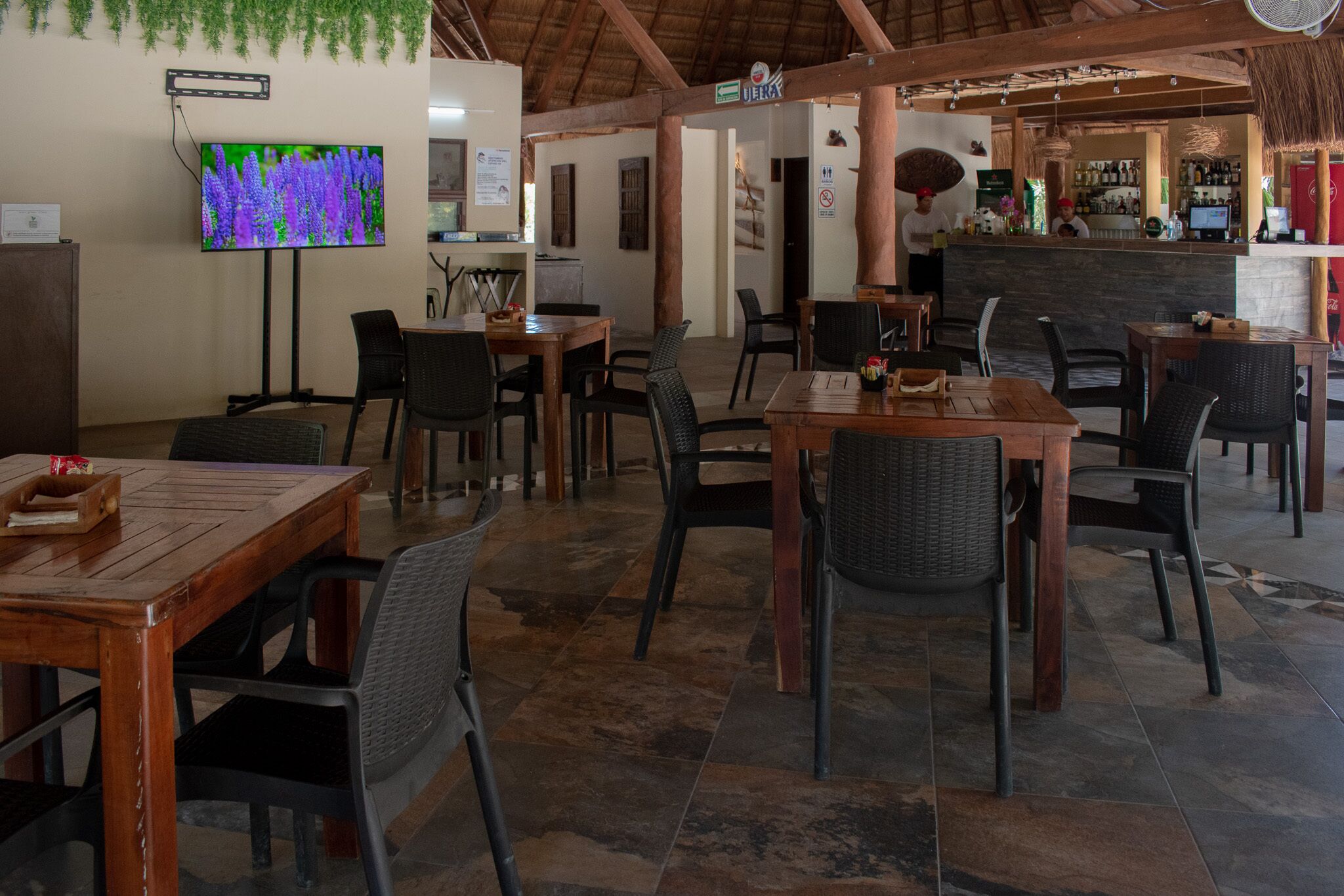A restaurant with wooden tables and chairs, a TV mounted on the wall, and a bar area in the background.