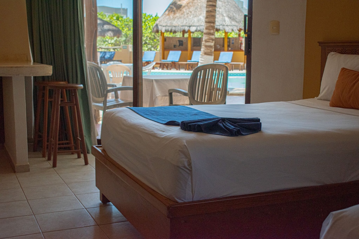 A hotel room with a bed, a desk, and a view of a pool area with lounge chairs.