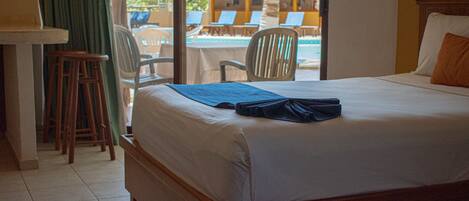 Habitación de hotel con cama, escritorio y vista a un área de piscina con sillas de descanso.