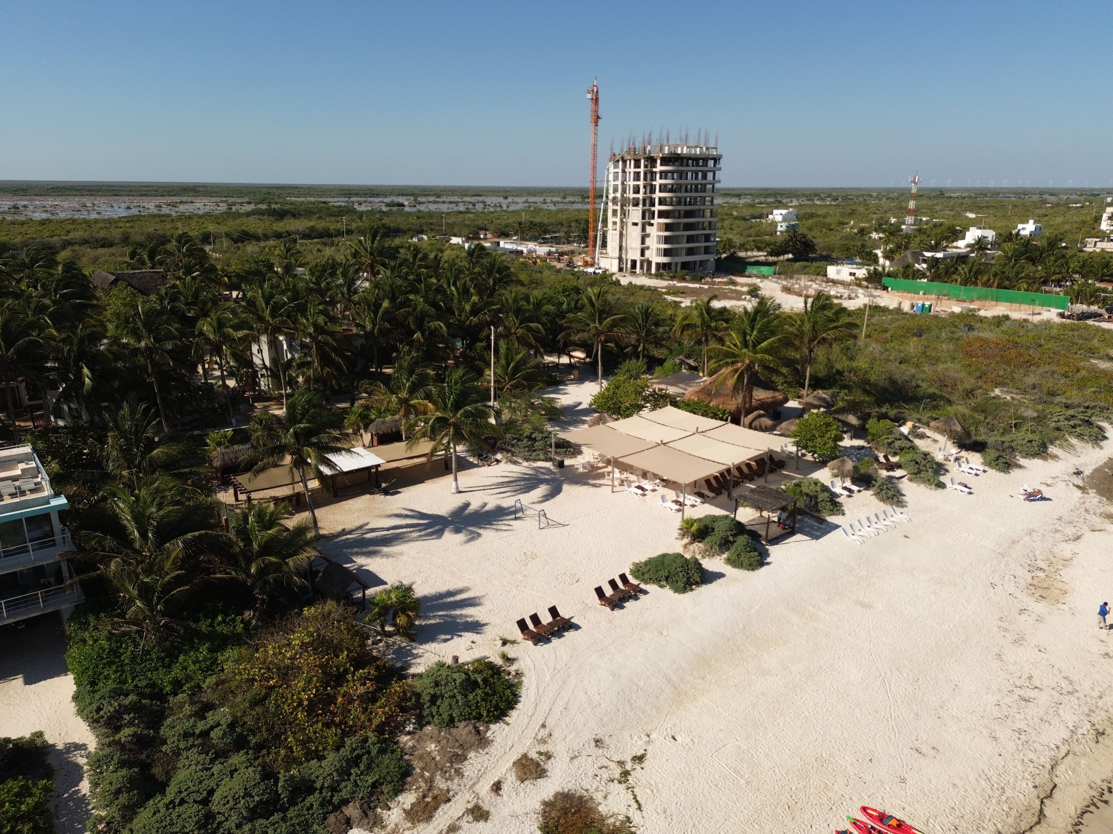 Un complexe hôtelier en bord de mer, avec des palmiers, une plage de sable et un bâtiment en construction.