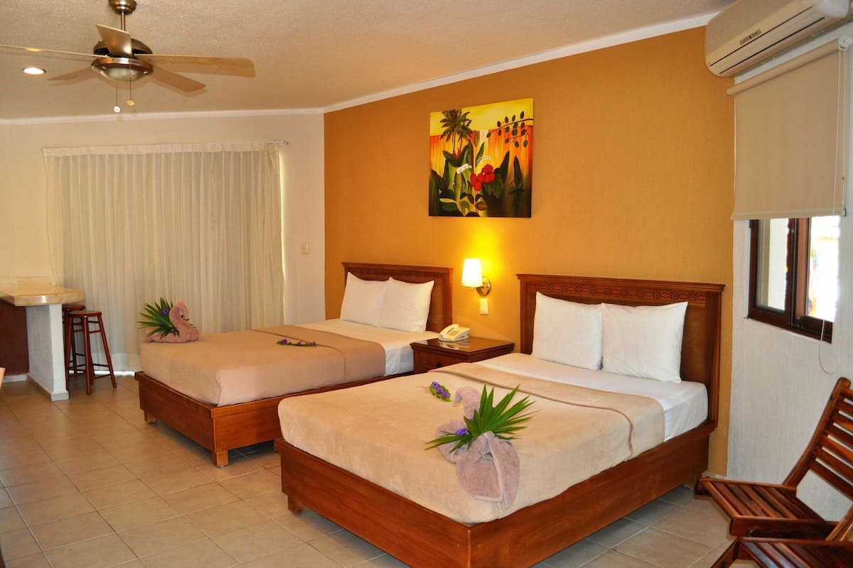 A hotel room with two beds, a desk, a chair, a ceiling fan, and an air conditioning unit.