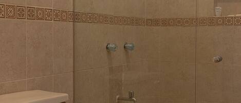 A bathroom with a glass-enclosed shower, a toilet, and a tiled floor.