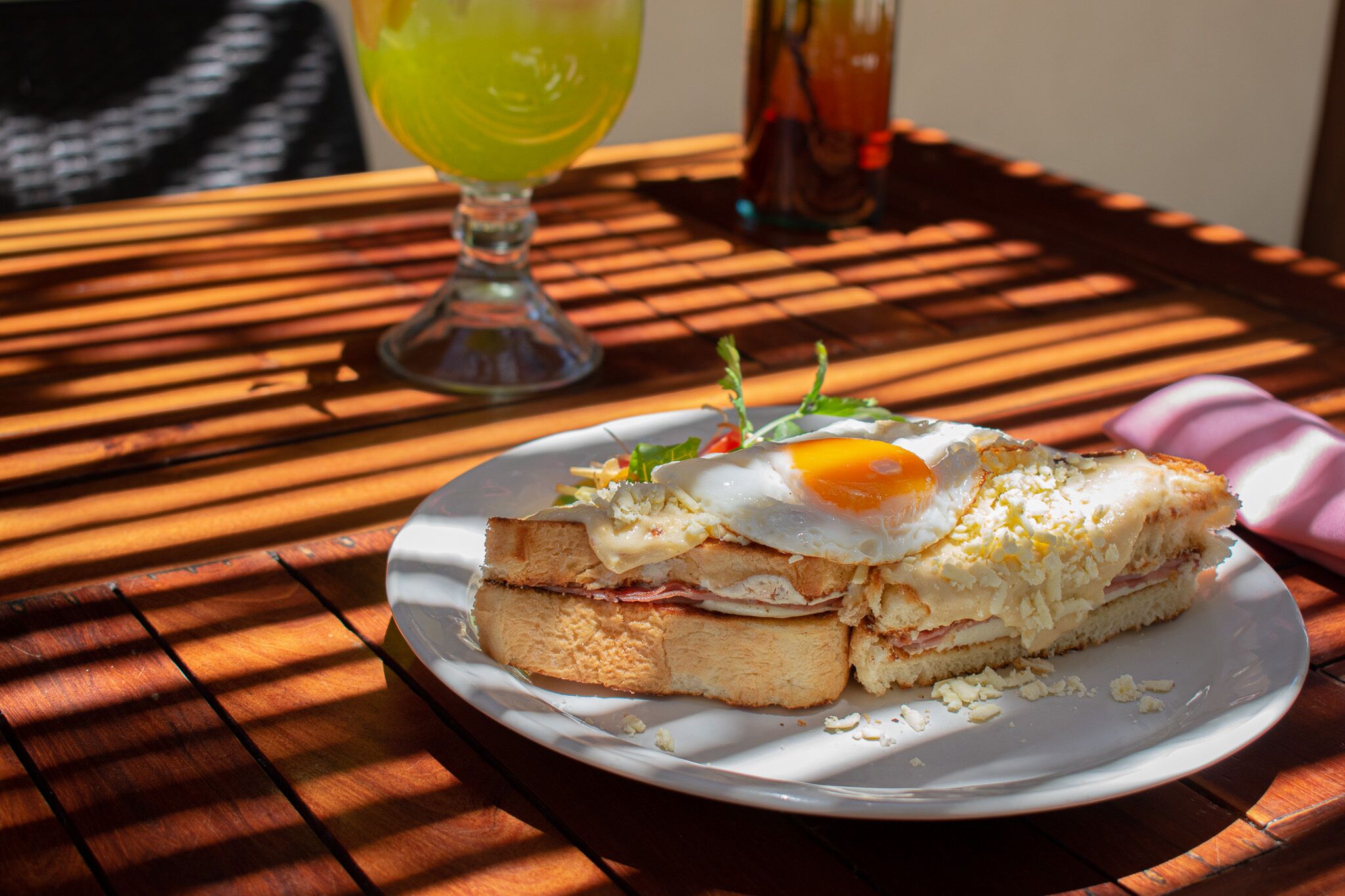 A sandwich with an egg on a white plate on a wooden table.