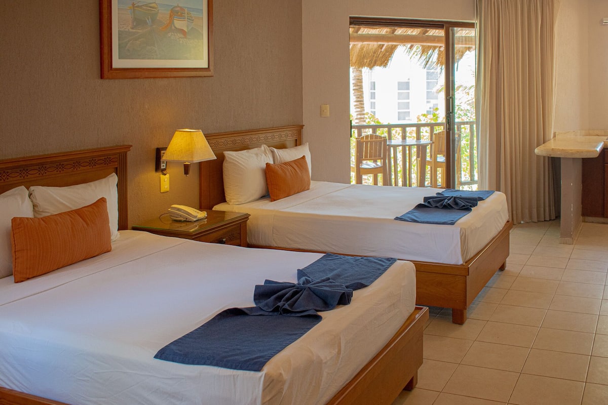 A hotel room with two beds, a nightstand with a lamp, a painting on the wall, and a view of the outside balcony.