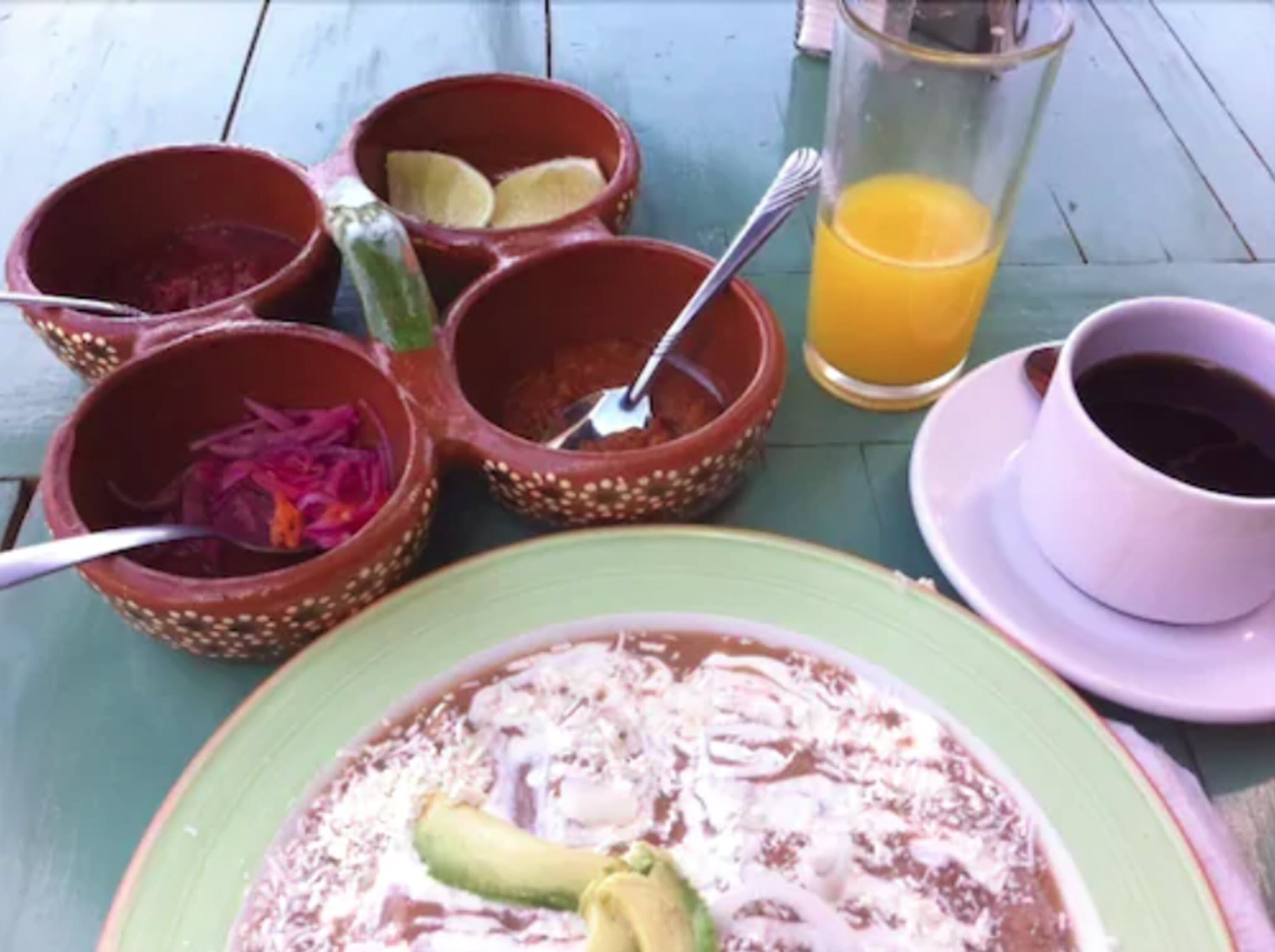 A table with a green plate, a cup of coffee, a glass of orange juice, and several small bowls with food items.