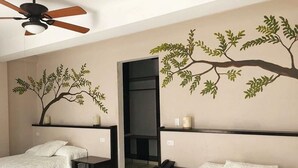 A hotel room with two beds, a ceiling fan, and wall art depicting trees. - Hotel Calli Quetzalcoatl (San Pedro Cholula)