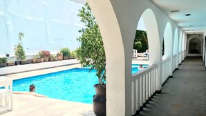 A covered swimming pool area with a tiled floor, white columns, and potted plants. - Hotel Calli Quetzalcoatl (San Pedro Cholula)