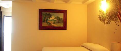 A bedroom with a bed, a painting on the wall, and a nightstand with a lamp.