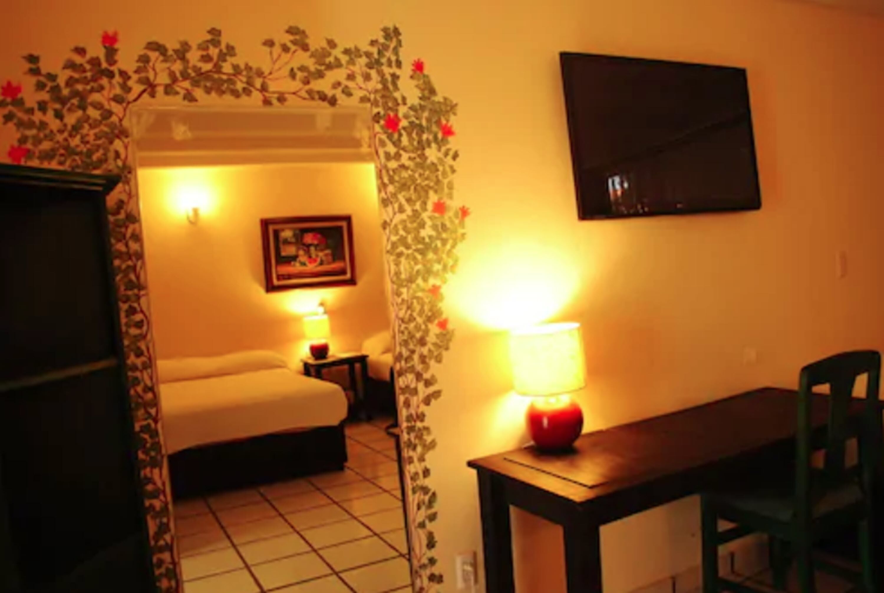 Habitación de hotel con cama, escritorio, silla, televisor en la pared y lámpara.