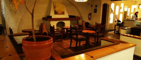 A cozy interior with a fireplace, wooden furniture, and a large terracotta pot.
