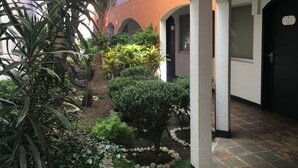 A courtyard with a stone pathway, potted plants, and a building with arches and a door marked '115'. - Hotel Calli Quetzalcoatl (San Pedro Cholula)