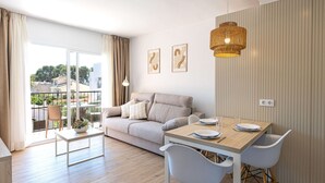 A modern living room with a sofa, dining table, and chairs. There is a balcony with a view of the outside. - Martinez Apartments (Calvia)