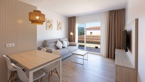A modern living room with a sofa, dining table, chairs, and a TV. - Martinez Apartments (Calvia)