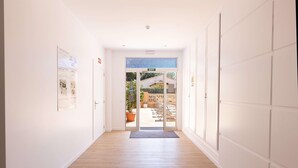 A hallway with a wooden floor, white walls, and a glass door leading outside. - Martinez Apartments (Calvia)