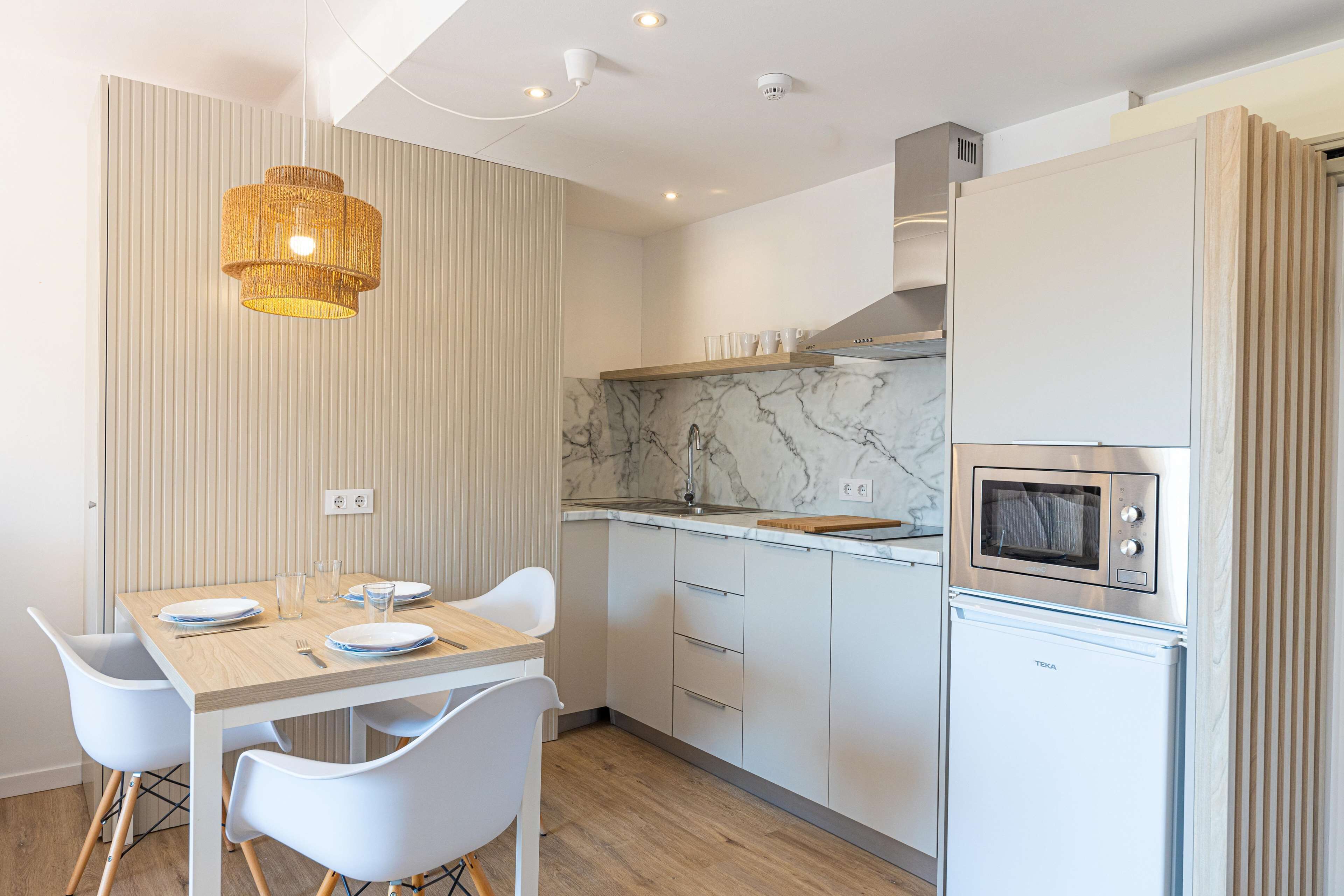 Een moderne keuken met een houten tafel, witte stoelen, een inbouwoven en een marmeren achterwand.