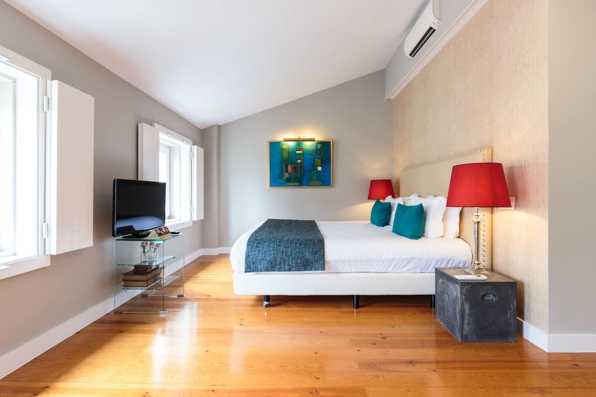 Un dormitorio moderno con cama, lámparas de noche, un televisor sobre una mesa de vidrio y un cuadro en la pared.