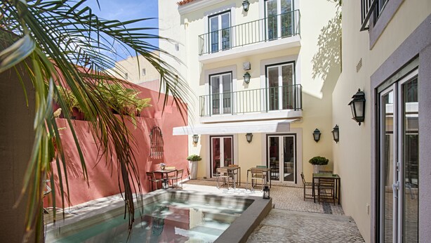 Un patio con piscina, mobiliario exterior y un edificio con balcones.